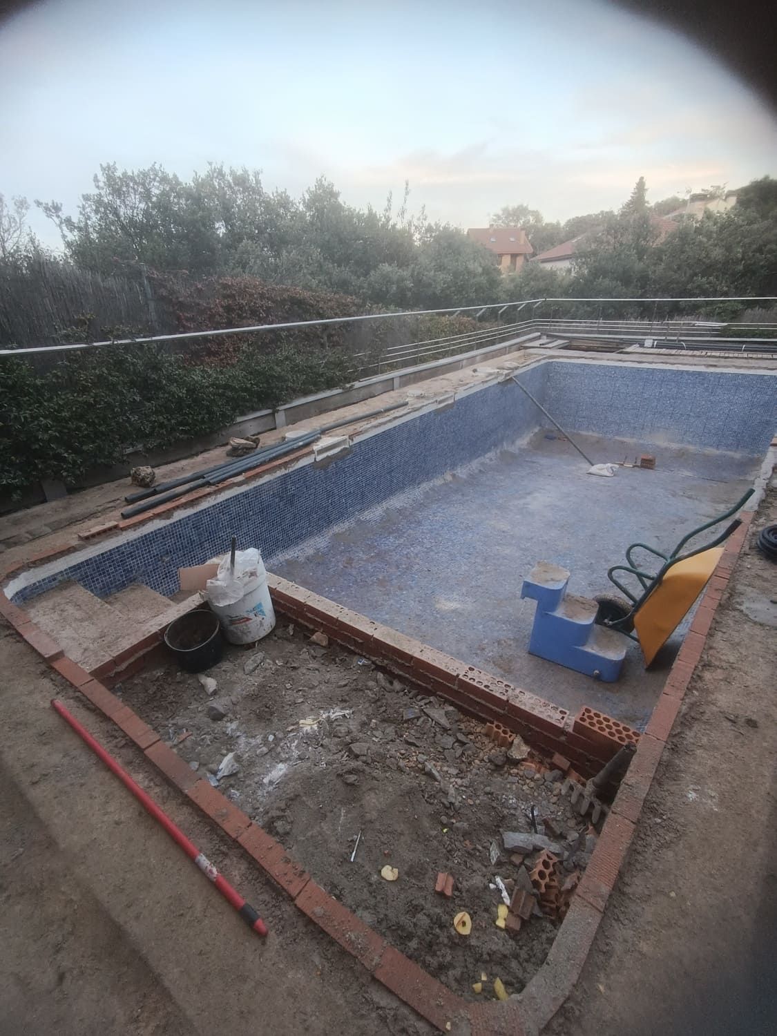 Piscina en construcción con azulejos azules, bordes de ladrillo rojo y herramientas de construcción.