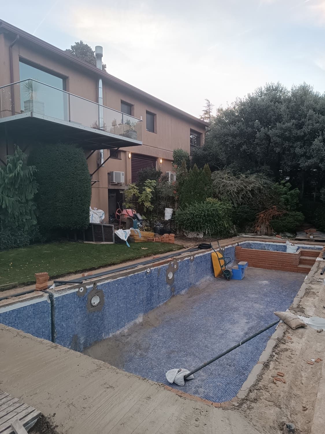 Piscina en construcción en un patio junto a una casa de dos plantas. Se ven azulejos azules en la piscina.