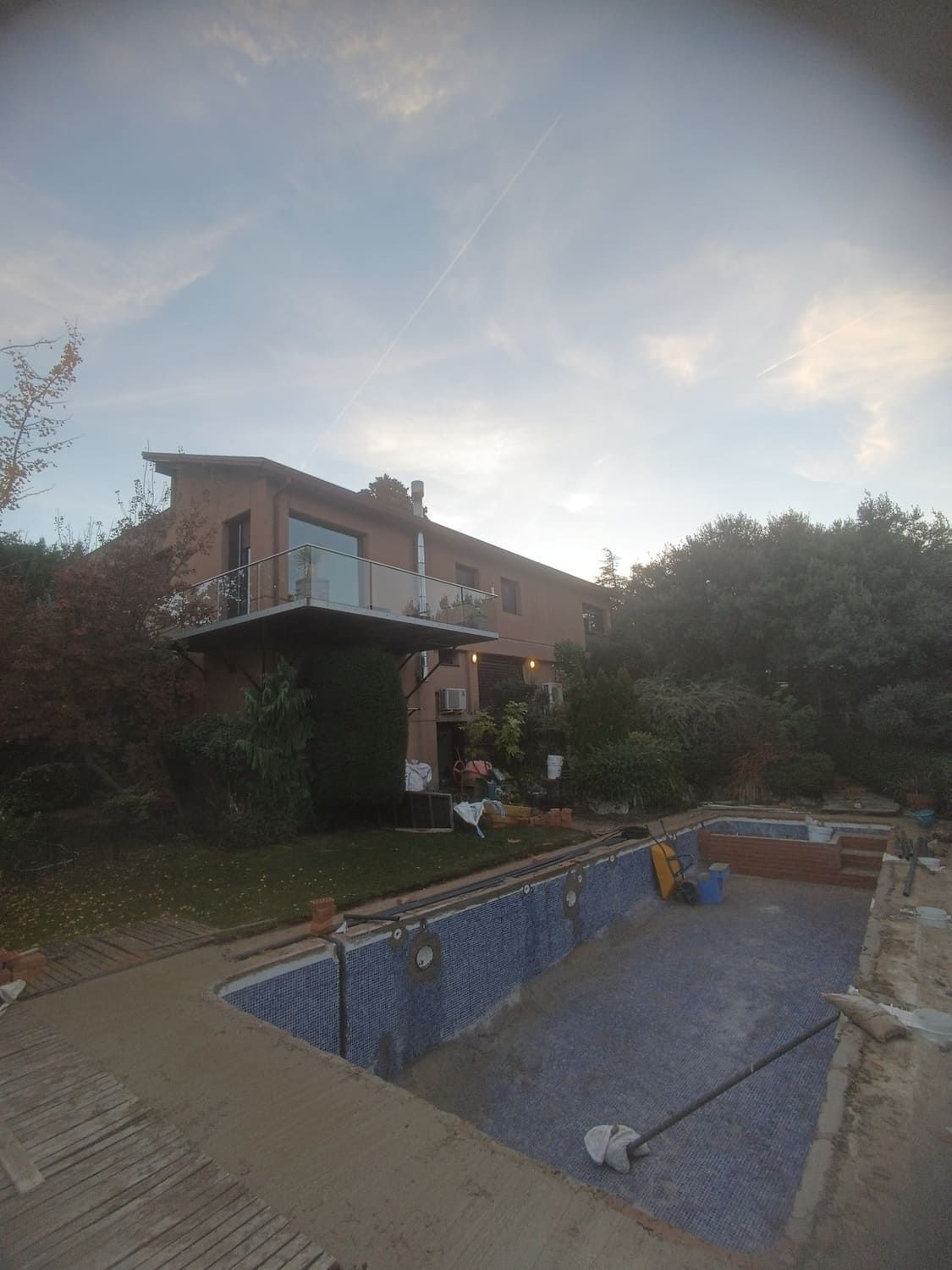 Piscina en construcción frente a una casa. Cielo nublado.