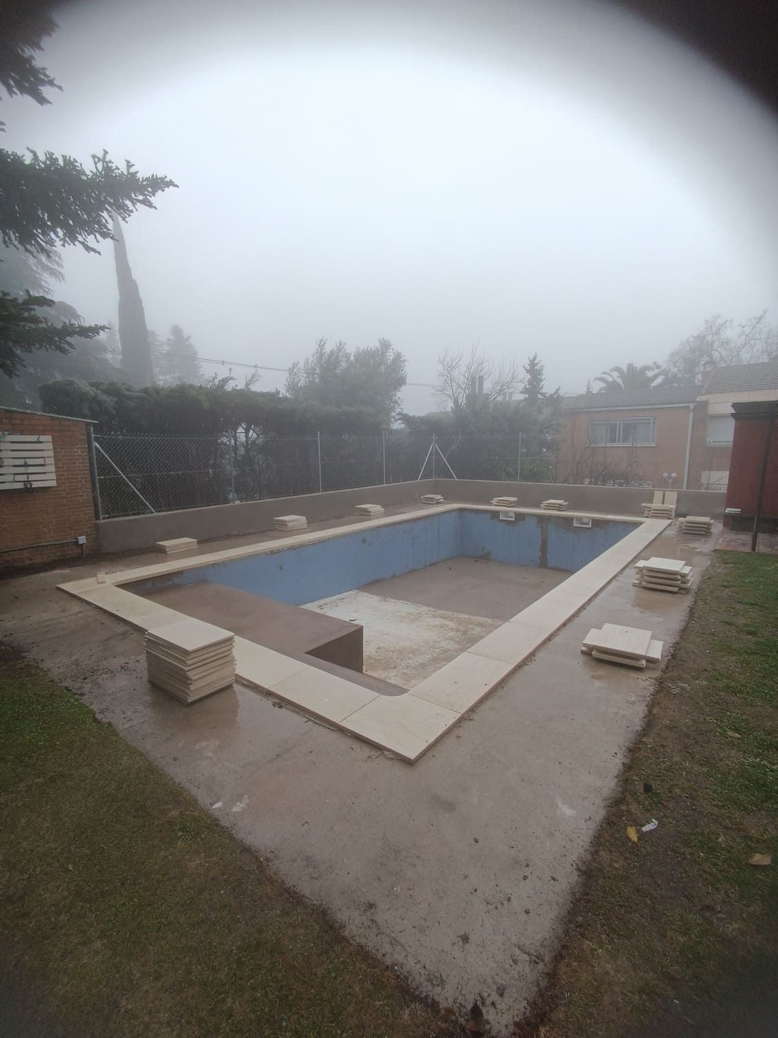 Piscina rectangular vacía en un día de niebla. Terraza de hormigón e interior de azulejos azules.