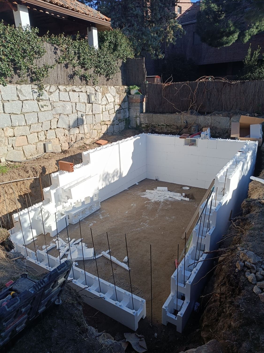 Construcción de piscina: Paredes de bloques de espuma blanca, piso de concreto, ubicada dentro de una excavación de tierra, con fondo de muro de contención.