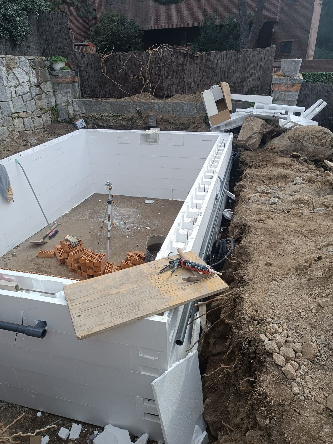 Construcción de la piscina: bloques de espuma blanca definen la forma de la piscina, rodeados de tierra y materiales de construcción.