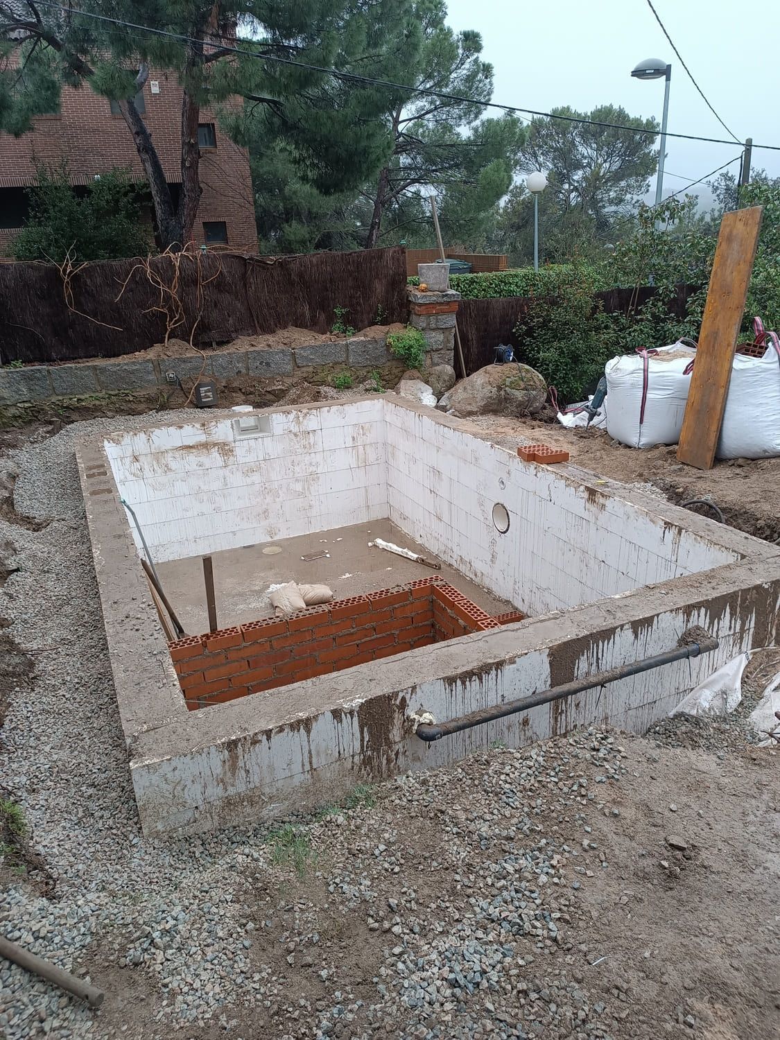 Estructura rectangular de hormigón en construcción, parcialmente cerrada con ladrillo, rodeada de grava.