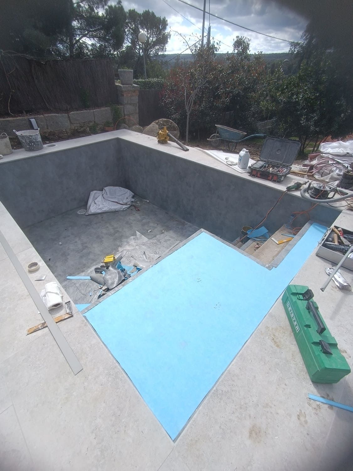 Piscina en construcción; panel aislante azul sobre escalones de hormigón. Exterior con mucha luz solar.