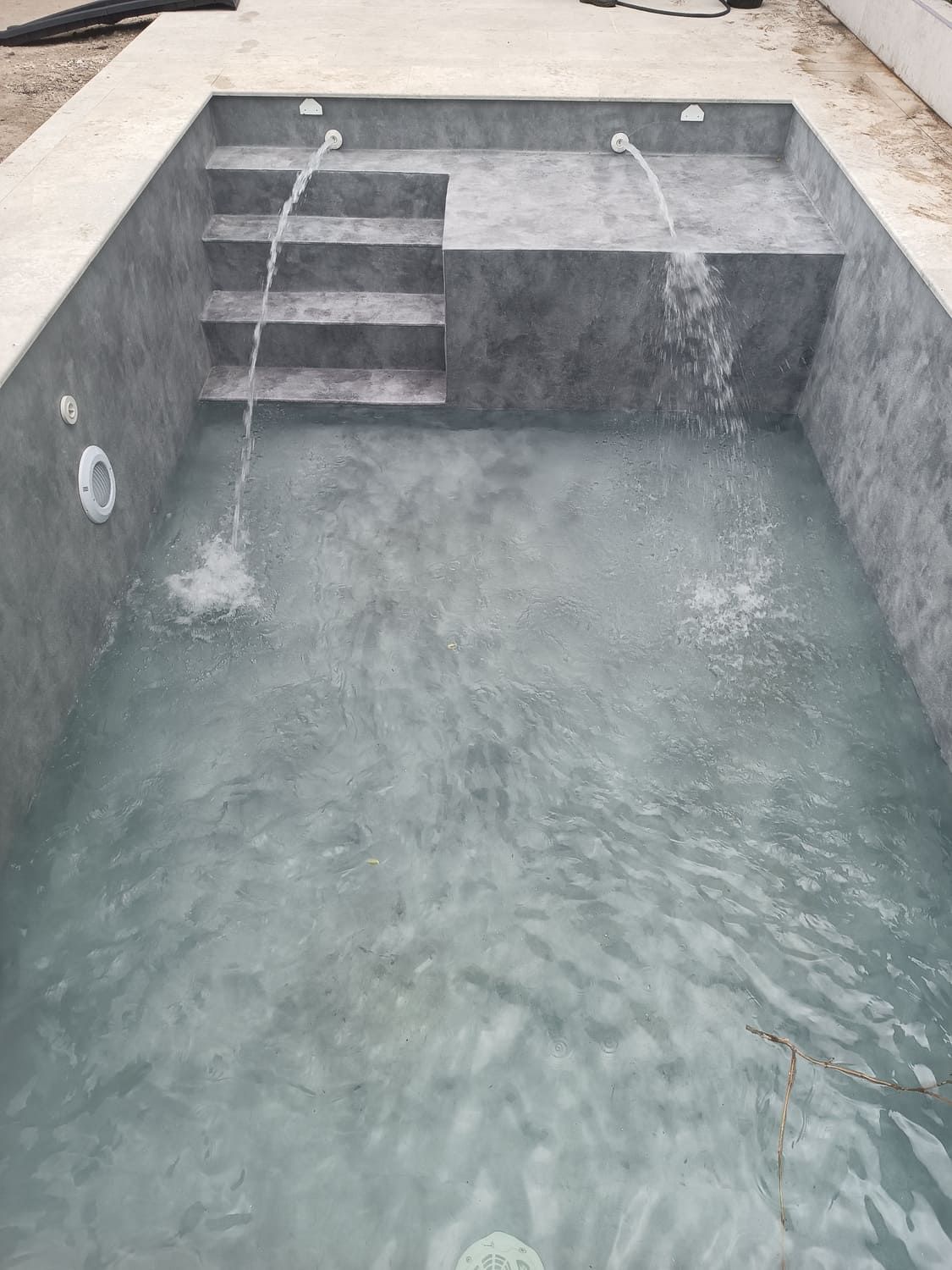 Piscina de hormigón gris con dos caños. Escaleras que bajan a la piscina.