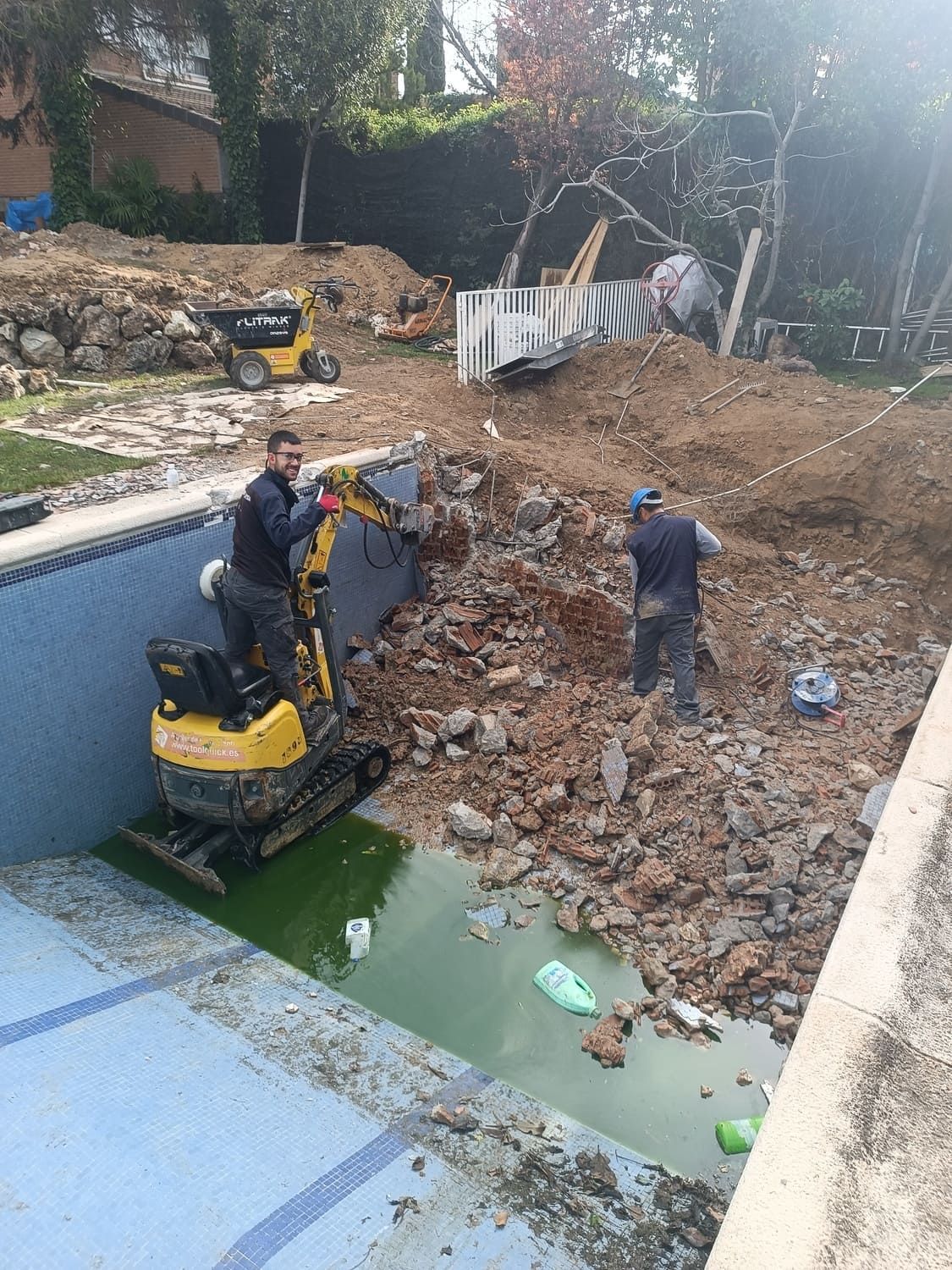Hombres y maquinaria excavan una piscina. La tierra se acumula. El agua verde la llena.