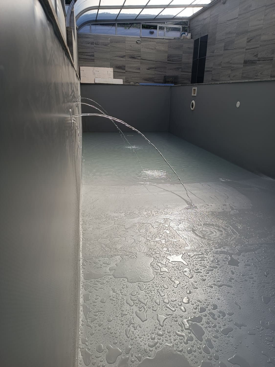 Piscina cubierta gris vacía con agua salpicando desde un lateral.