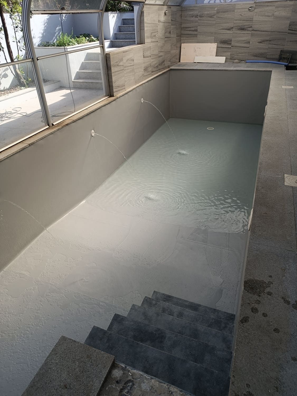 Piscina vacía, pintada de gris, con escaleras incorporadas, vista desde arriba.