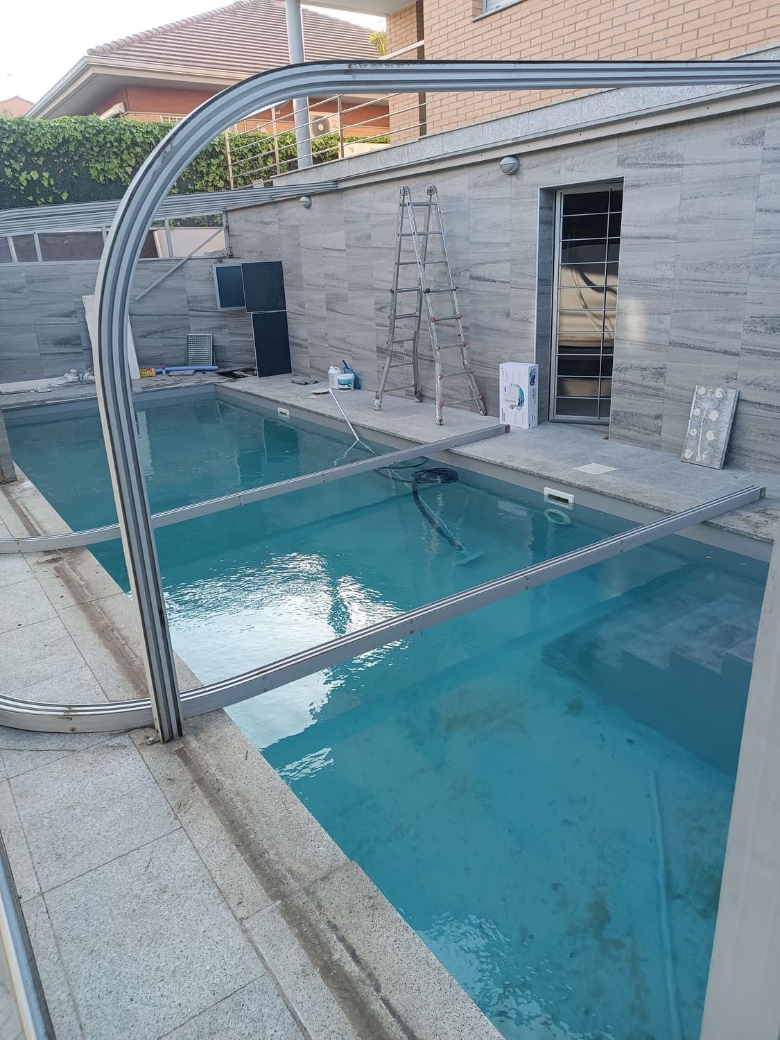 Piscina con estructura metálica parcialmente construida, agua azul y borde de baldosas grises.