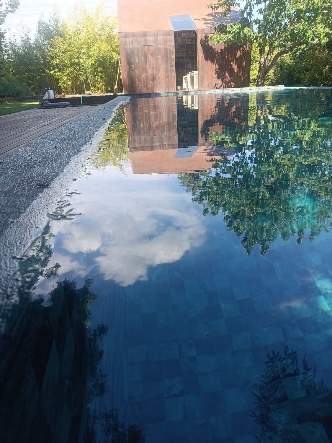 Piscina infinita que refleja un cielo nublado y un edificio de color óxido en una zona boscosa.