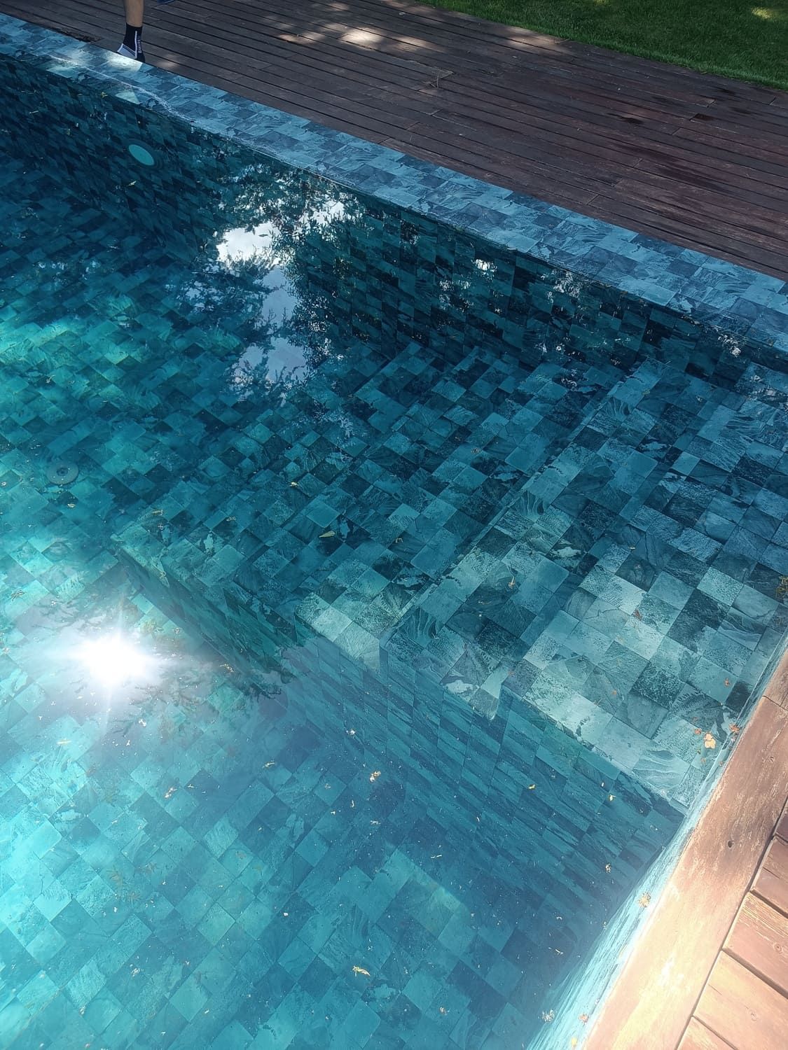 Piscina con escalones de baldosas turquesas y terraza de madera.