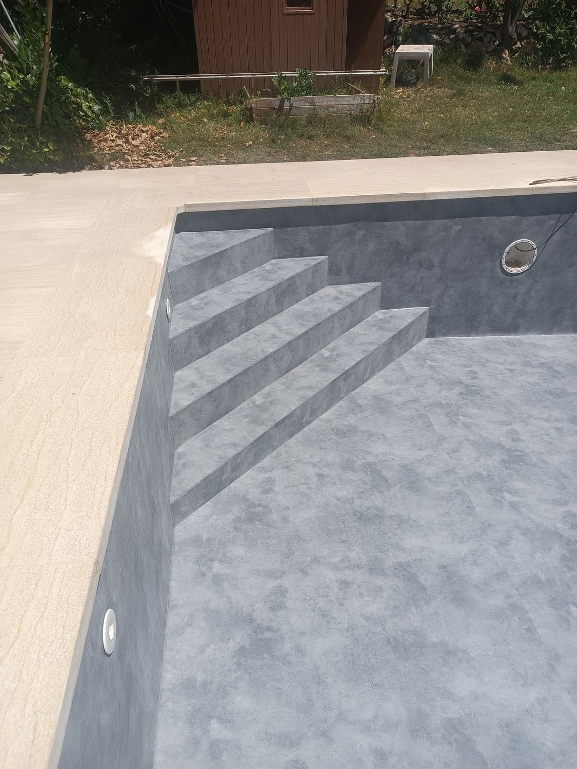 Interior de piscina gris con escalones, adyacente a un borde de hormigón beige.