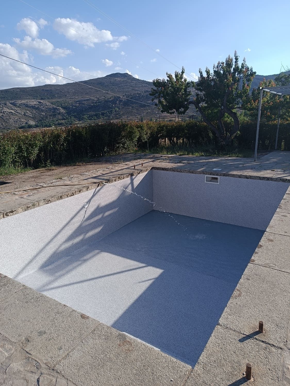 Piscina de hormigón vacía con lados de baldosas, interior azul, bajo un cielo azul brillante.