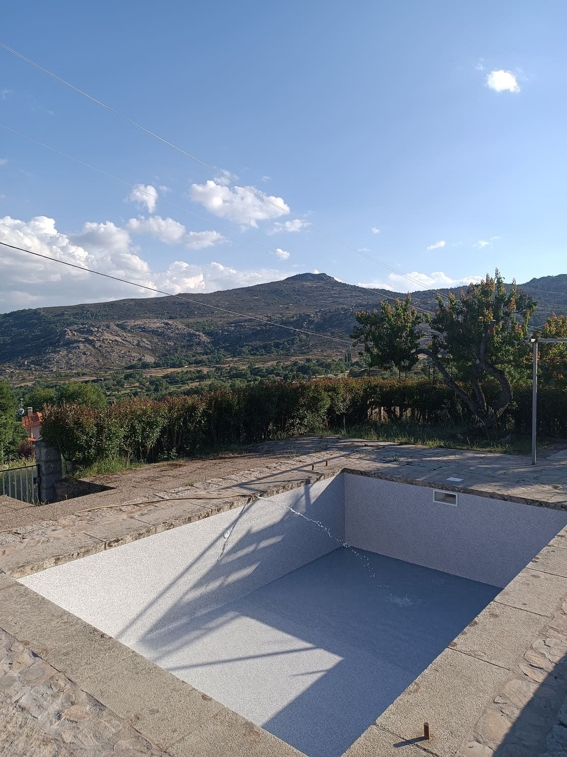 Piscina vacía con un interior de mosaico, con un telón de fondo de montañas y un cielo azul.