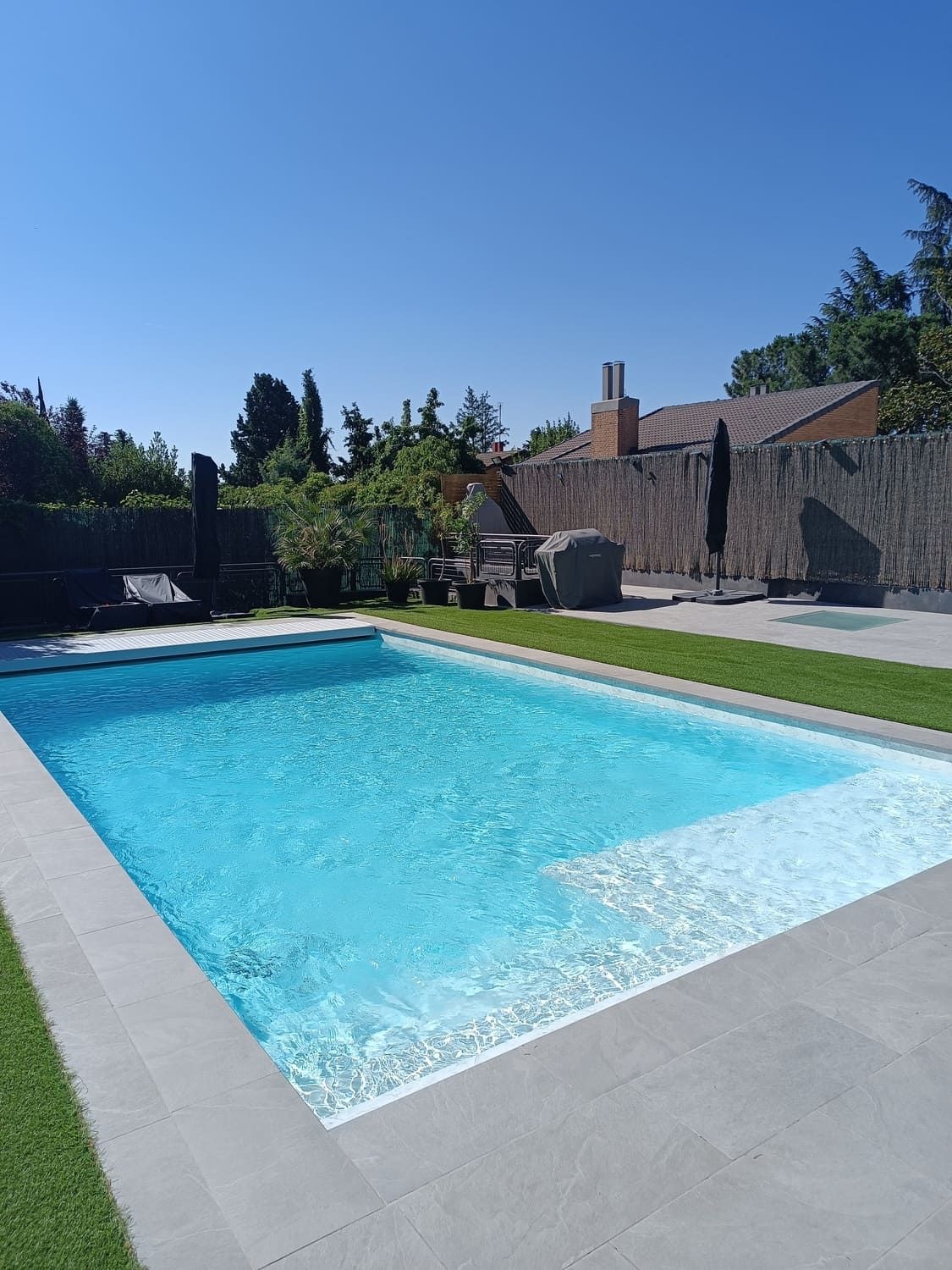 Piscina rectangular con agua azul cristalina y patio de hormigón bajo un cielo soleado.
