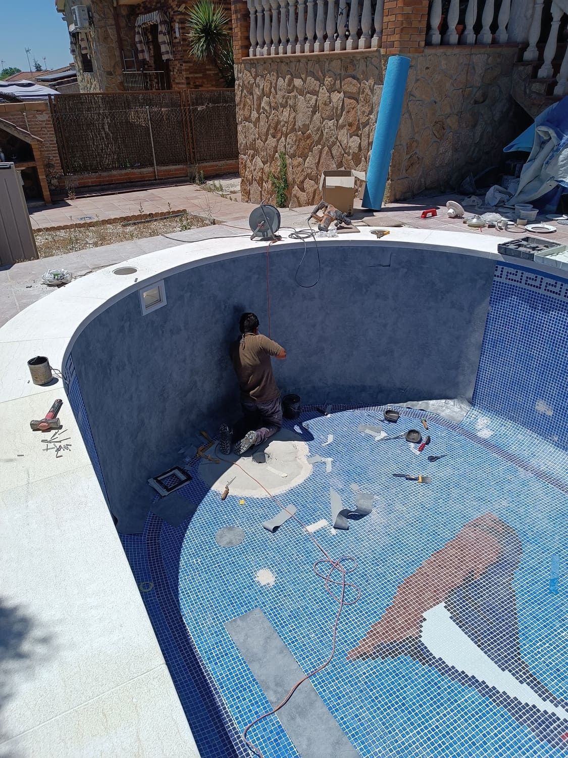 Persona trabajando en una piscina de azulejos azules. Piscina en construcción. Exterior.