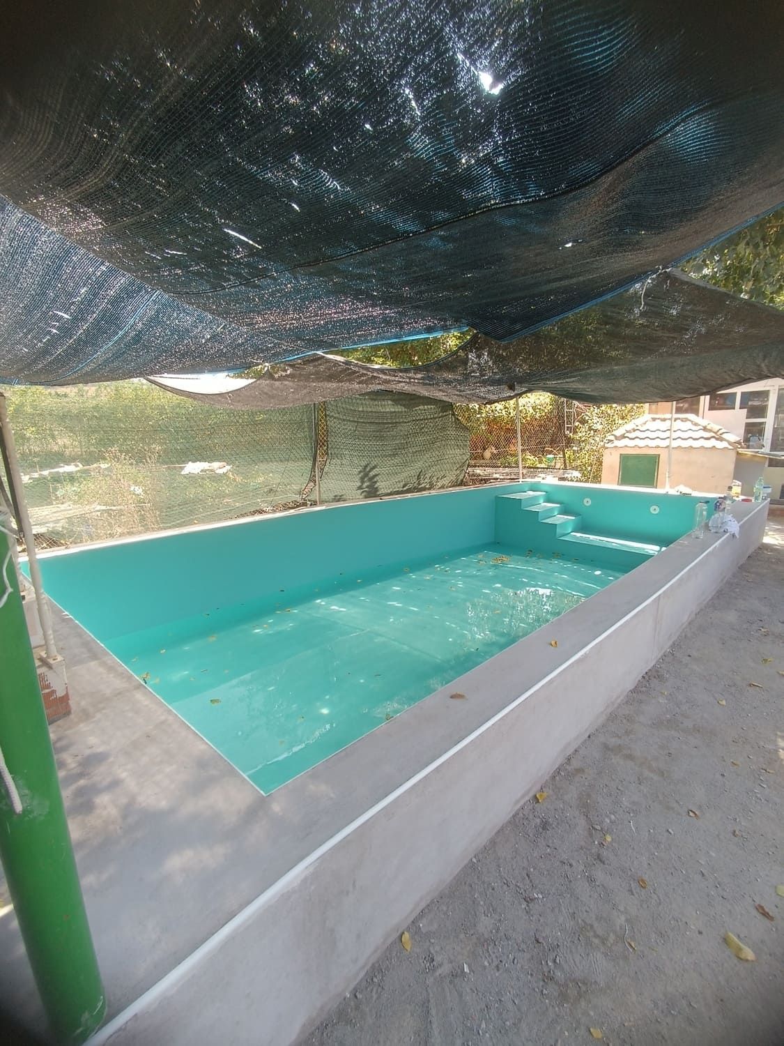 Piscina de agua azul con escalones, cubierta con una malla negra. La piscina está rodeada de hormigón.