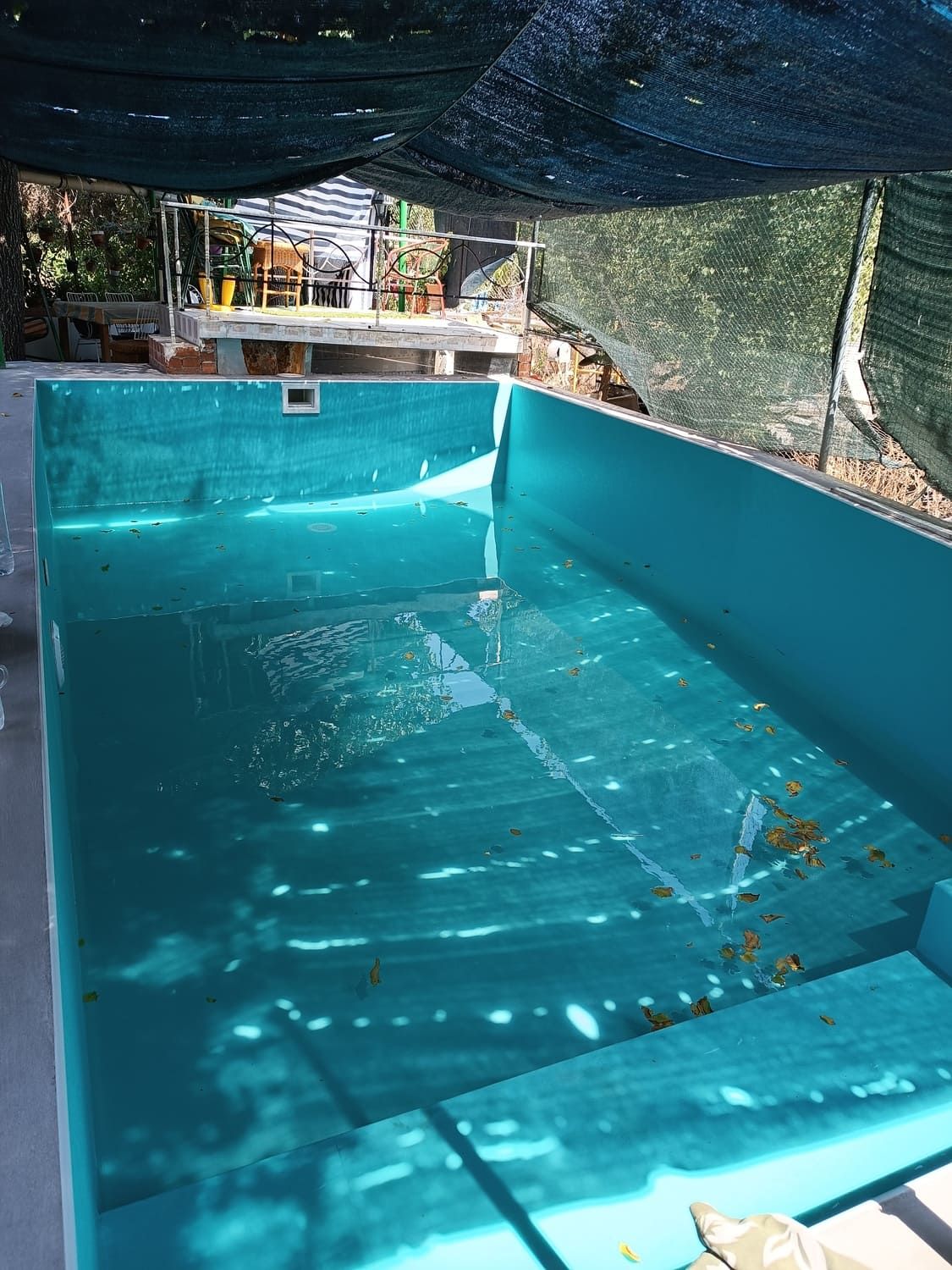 Piscina azul vacía bajo un dosel sombreado.