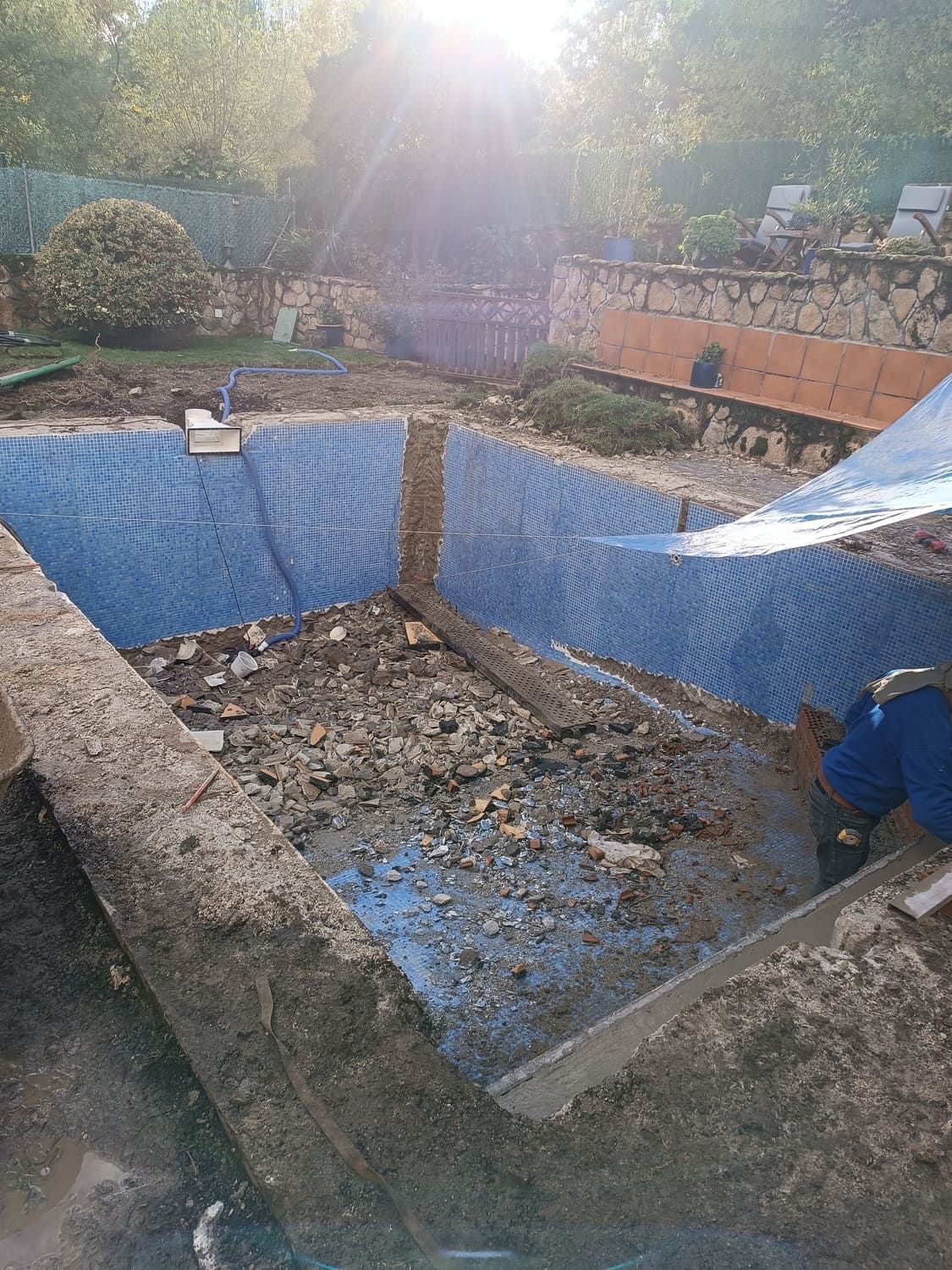 Sitio de construcción con malla azul que recubre un pozo rectangular, con luz solar arriba.
