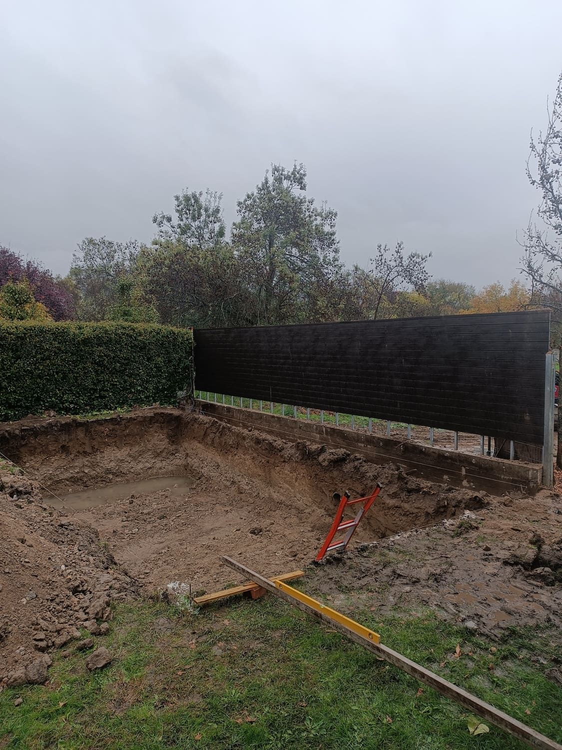 Una sección excavada en un patio con césped, al lado de una cerca de madera bajo un cielo nublado.