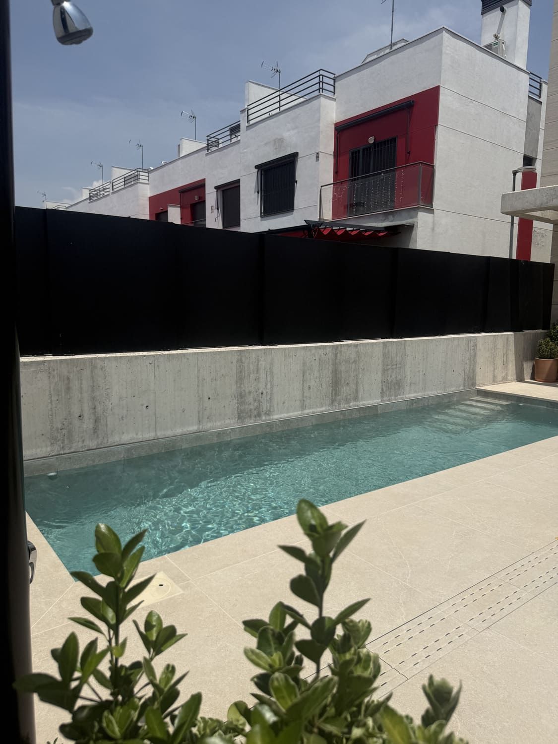 Una piscina estrecha frente a casas adosadas modernas con detalles en rojo y una cerca negra para mayor privacidad.