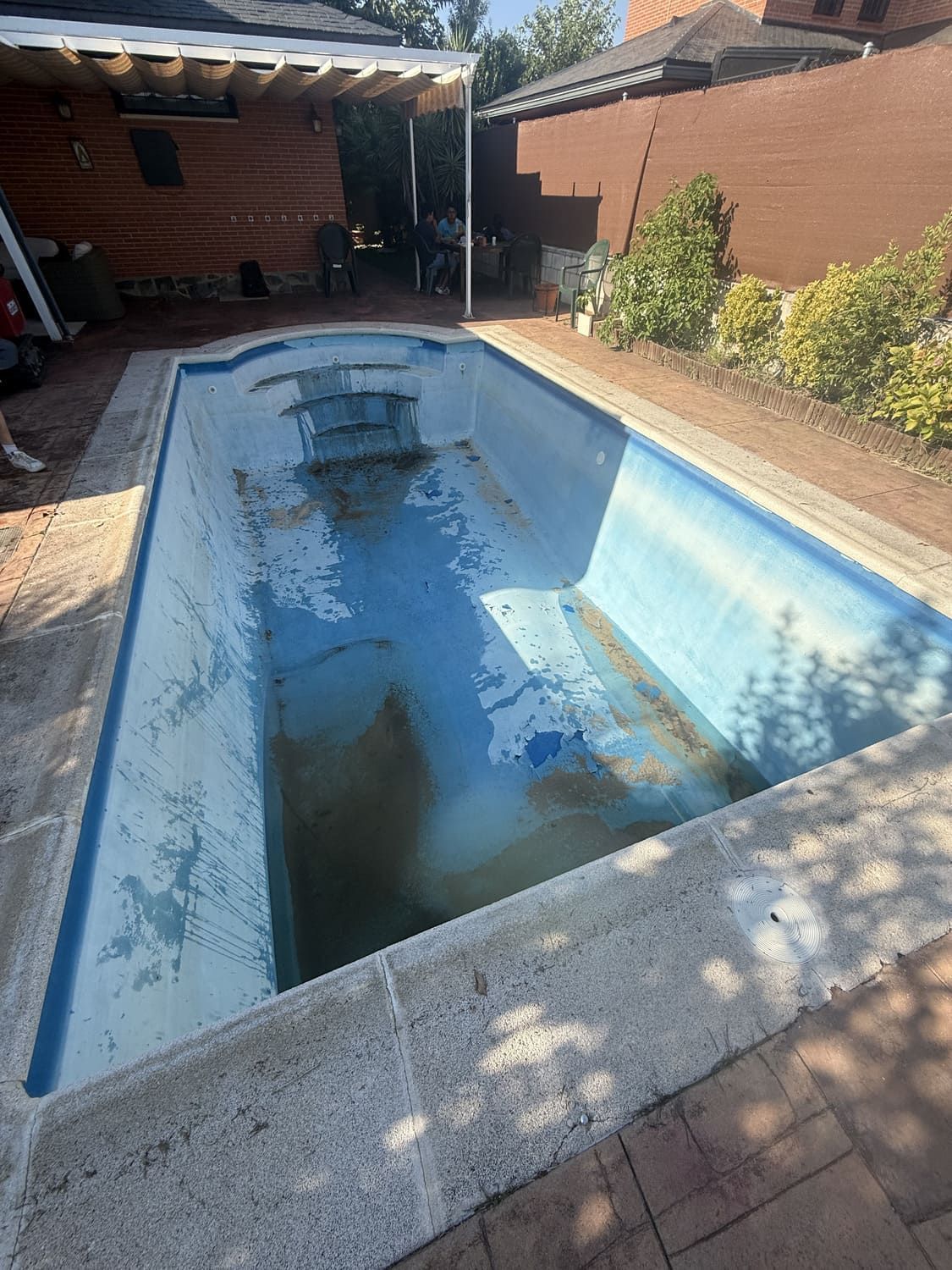 Piscina rectangular vacía con interior azul sucio y borde de piedra.