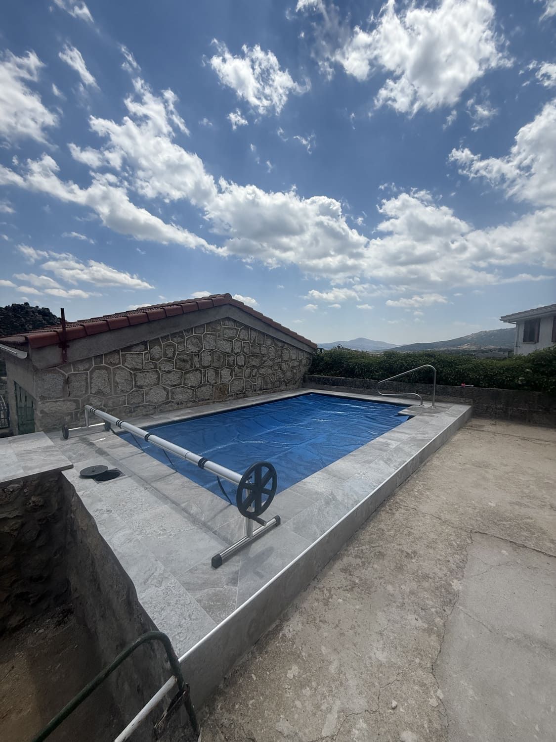 Piscina con cubierta azul, junto a un edificio de piedra, bajo un cielo nublado.
