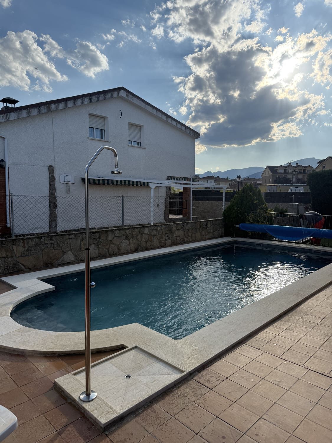 Una piscina frente a una casa blanca en un día soleado.