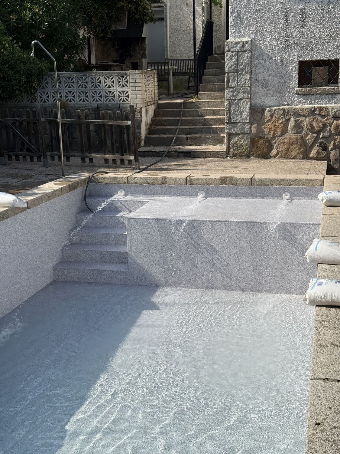 Piscina con escaleras, paredes de piedra y un edificio al fondo.
