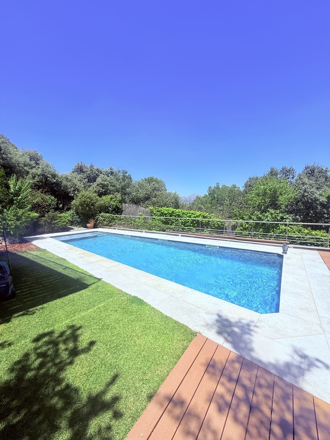 Piscina de agua azul rodeada de deck y césped verde bajo un cielo despejado.