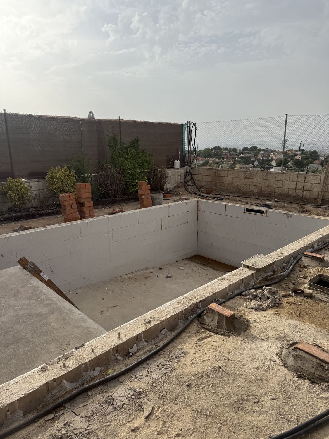 Piscina rectangular vacía en construcción en una azotea, con hormigón circundante y vistas al paisaje urbano.