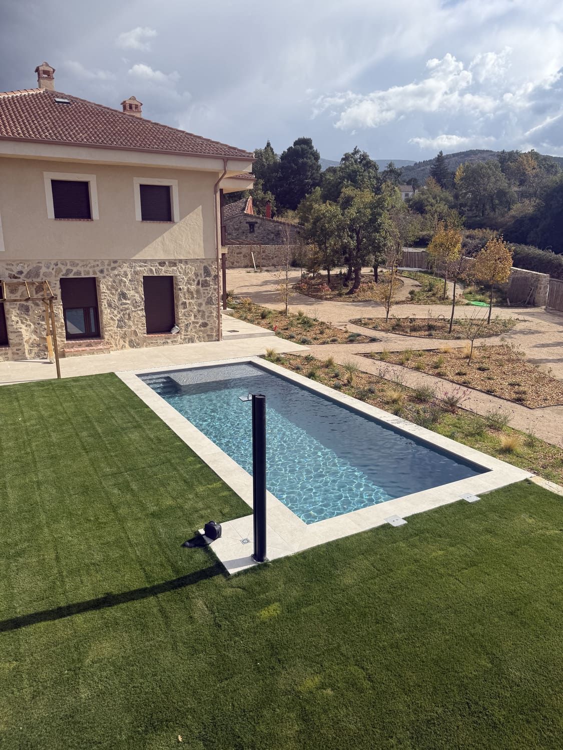 Una piscina rectangular con agua turquesa, rodeada de césped verde y un edificio de piedra en un día soleado.