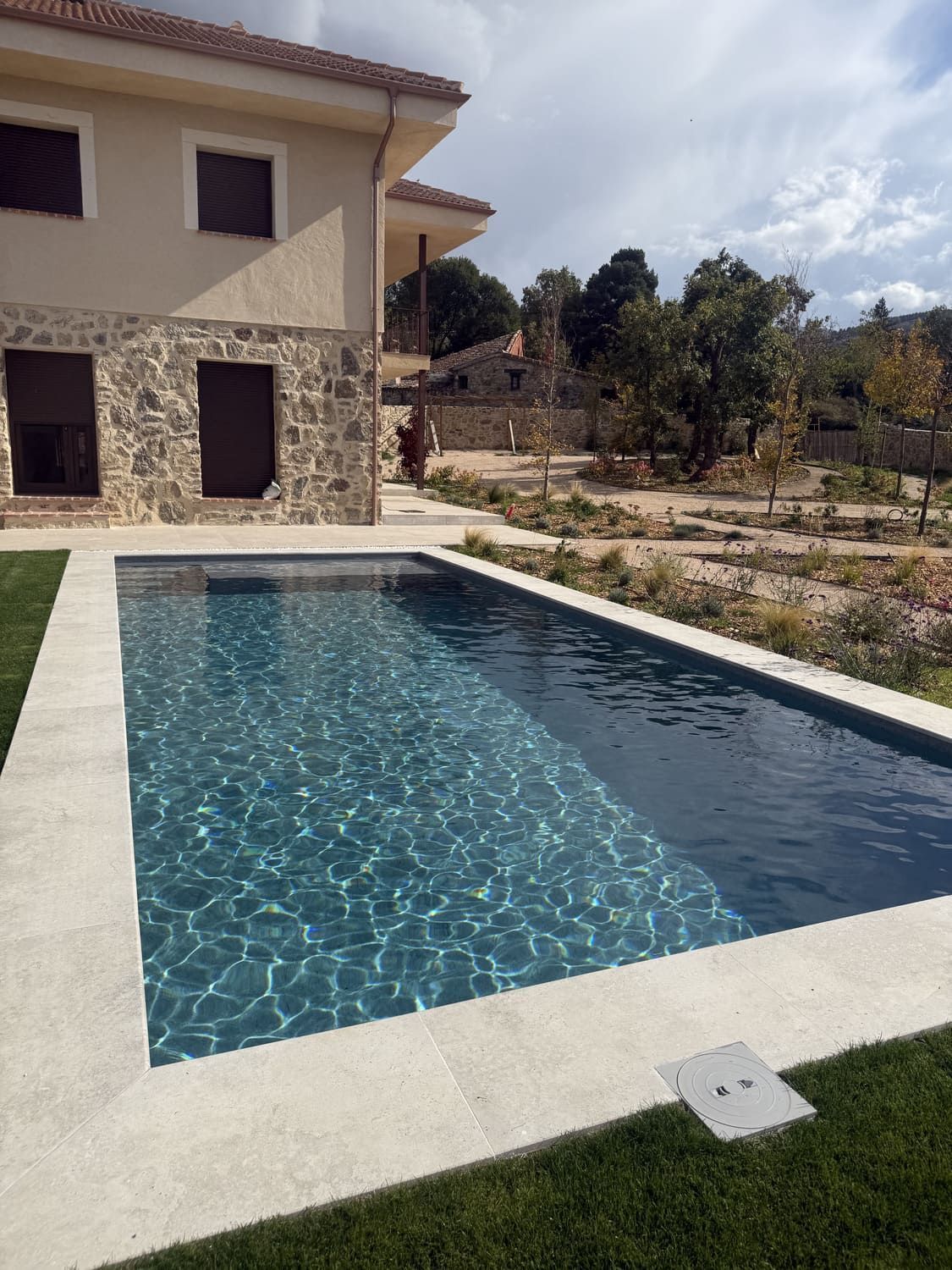 Piscina rectangular de agua turquesa, situada en un patio con una casa con fachada de piedra y color canela.