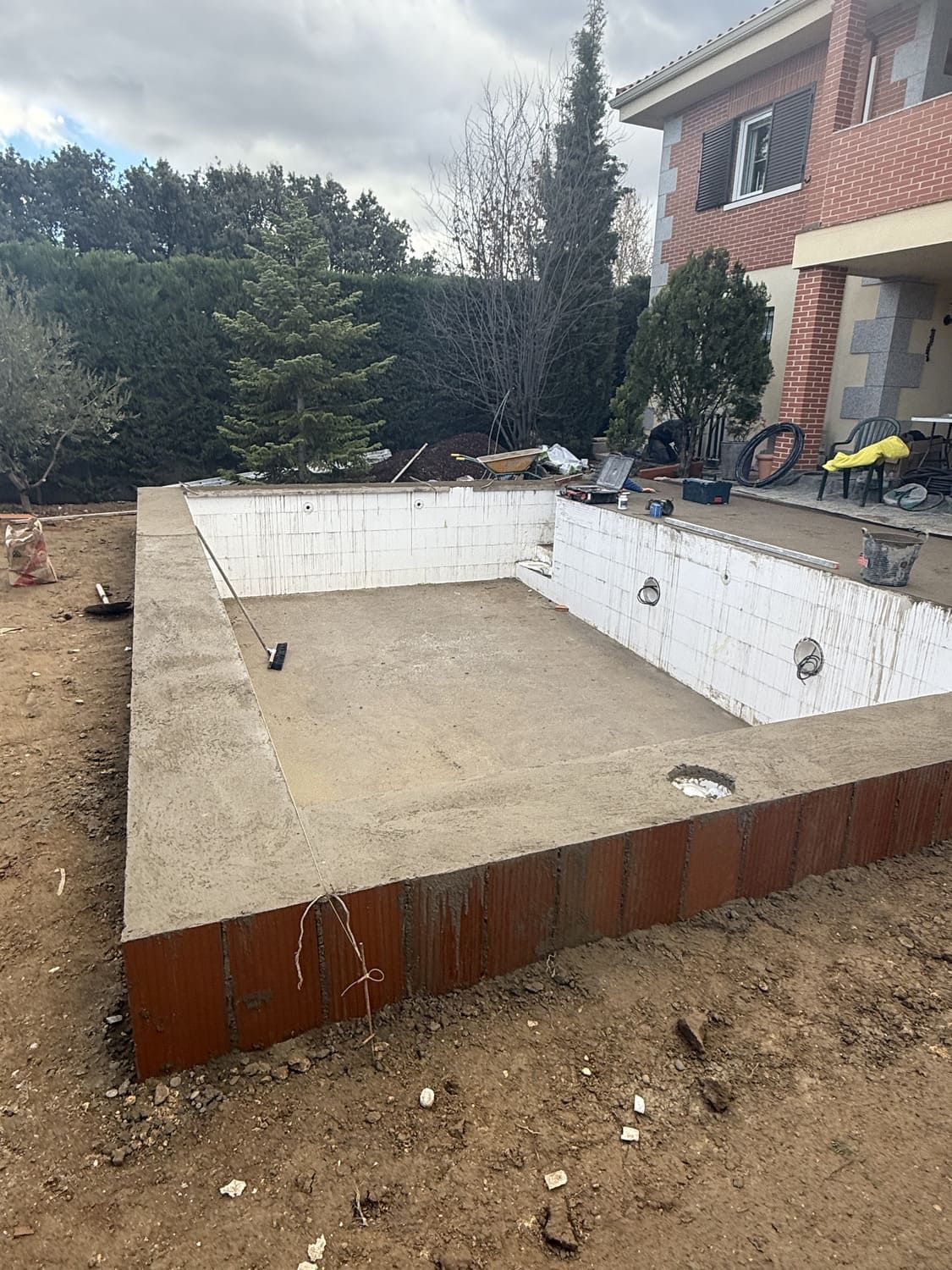 Piscina rectangular vacía en construcción, enmarcada por paredes de metal oxidado y bloques blancos.