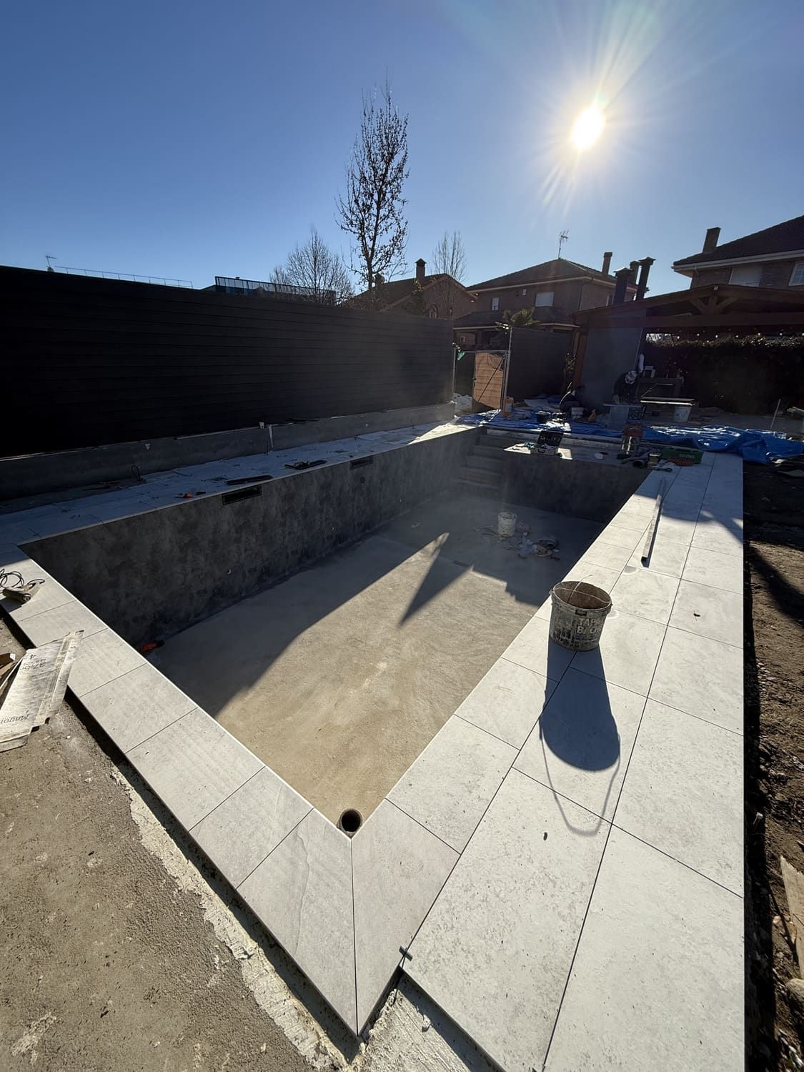 Sitio de construcción de una piscina en forma de V con borde de piedra, visto en un día soleado.