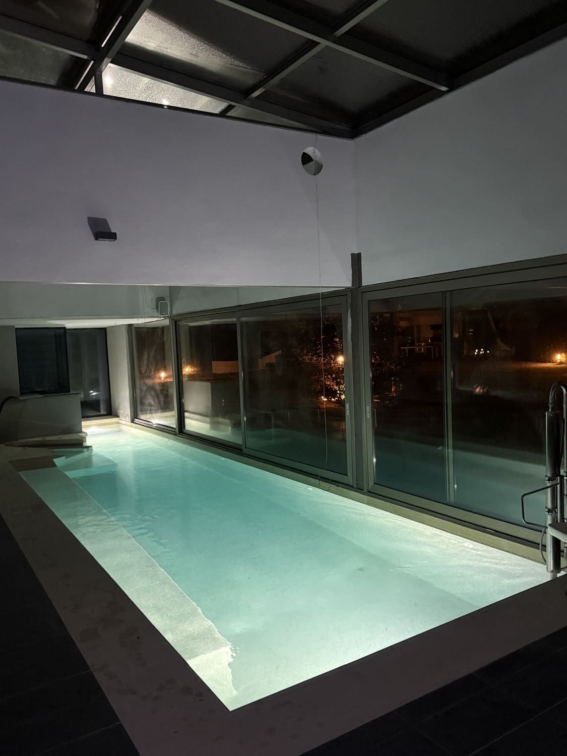Piscina cubierta rectangular con paredes de cristal por la noche.