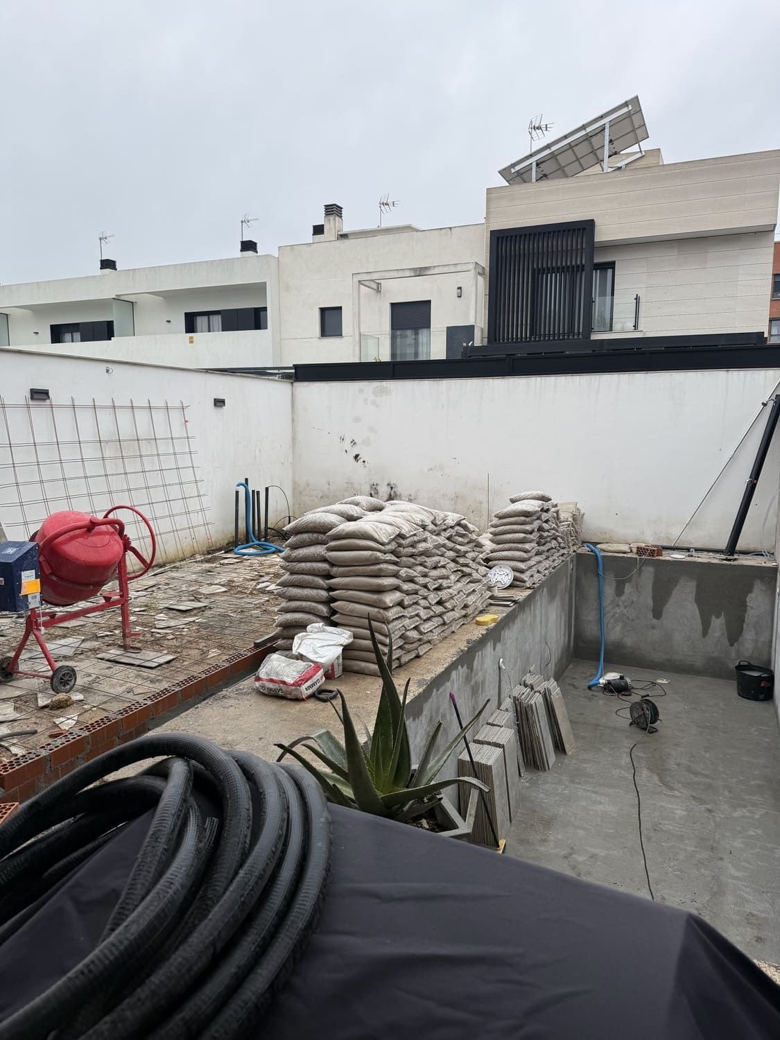 Obra en construcción con sacos de cemento, hormigonera y piscina en construcción.