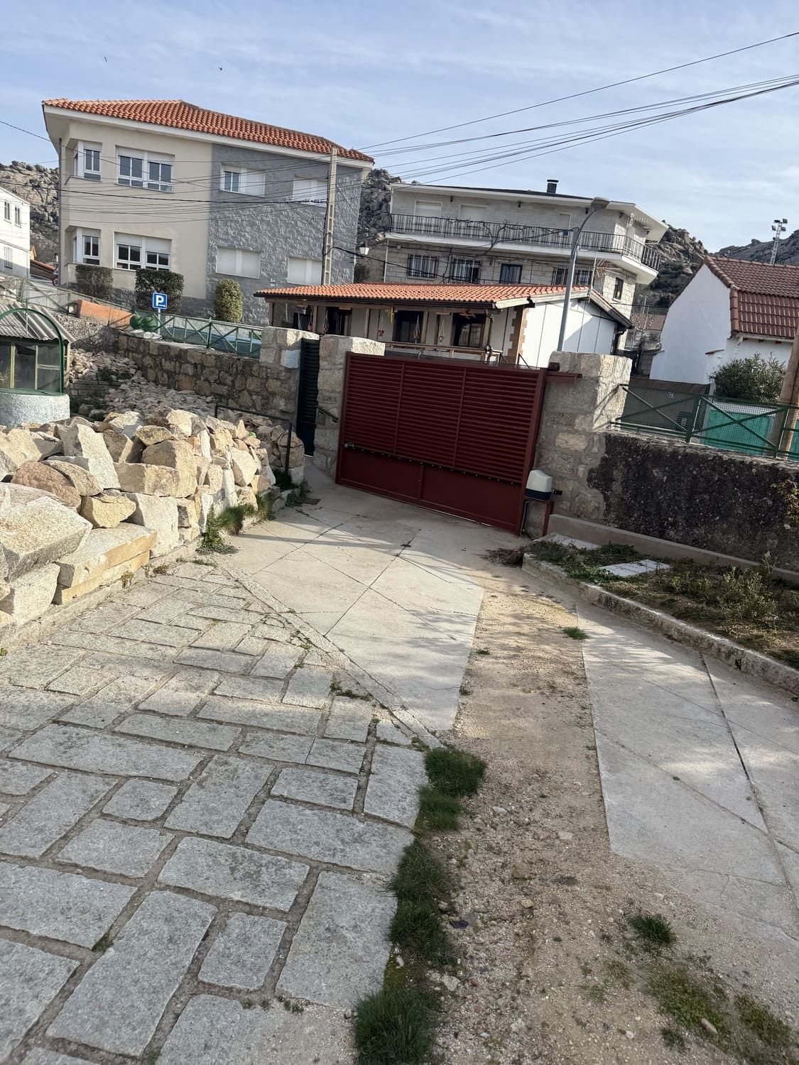 Un camino de piedra conduce a edificios con entrada con portones rojos bajo un cielo claro y soleado.