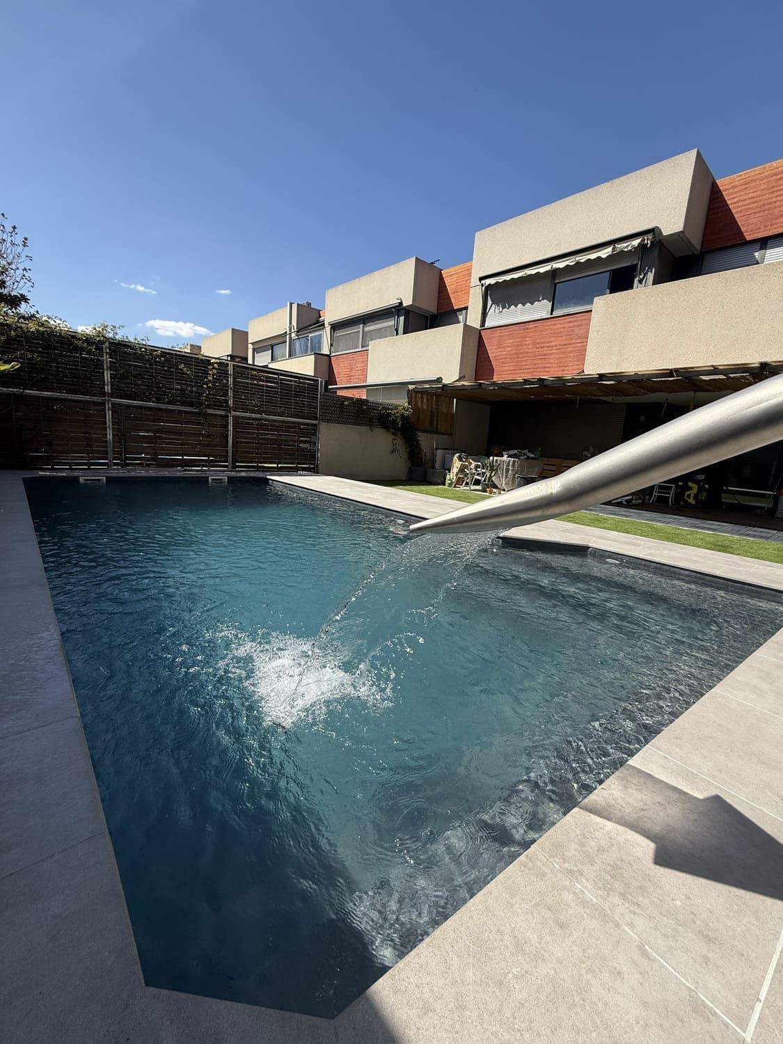 Piscina con fuente de agua, frente a un edificio moderno de ladrillo rojo, en un día soleado.