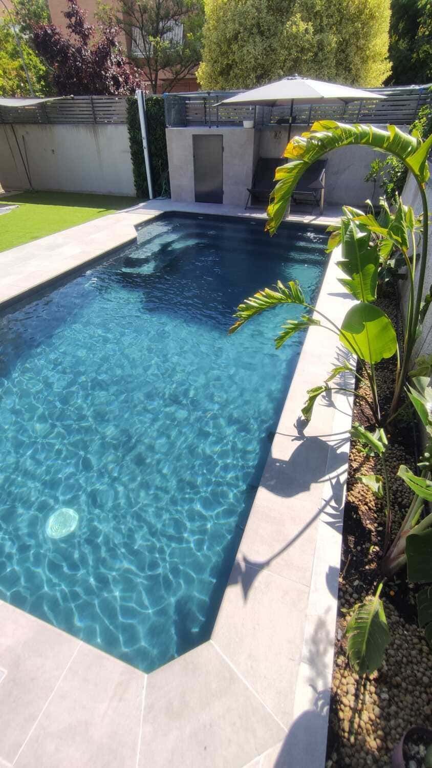 Piscina rectangular de agua turquesa, rodeada de piedra clara, escalones y vegetación.