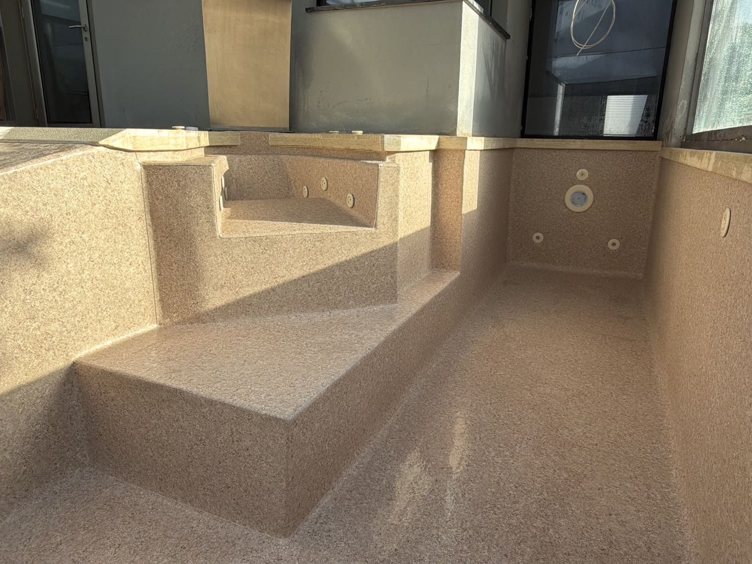 Piscina vacía enterrada con interior moteado de color canela, escalones incorporados y chorros.