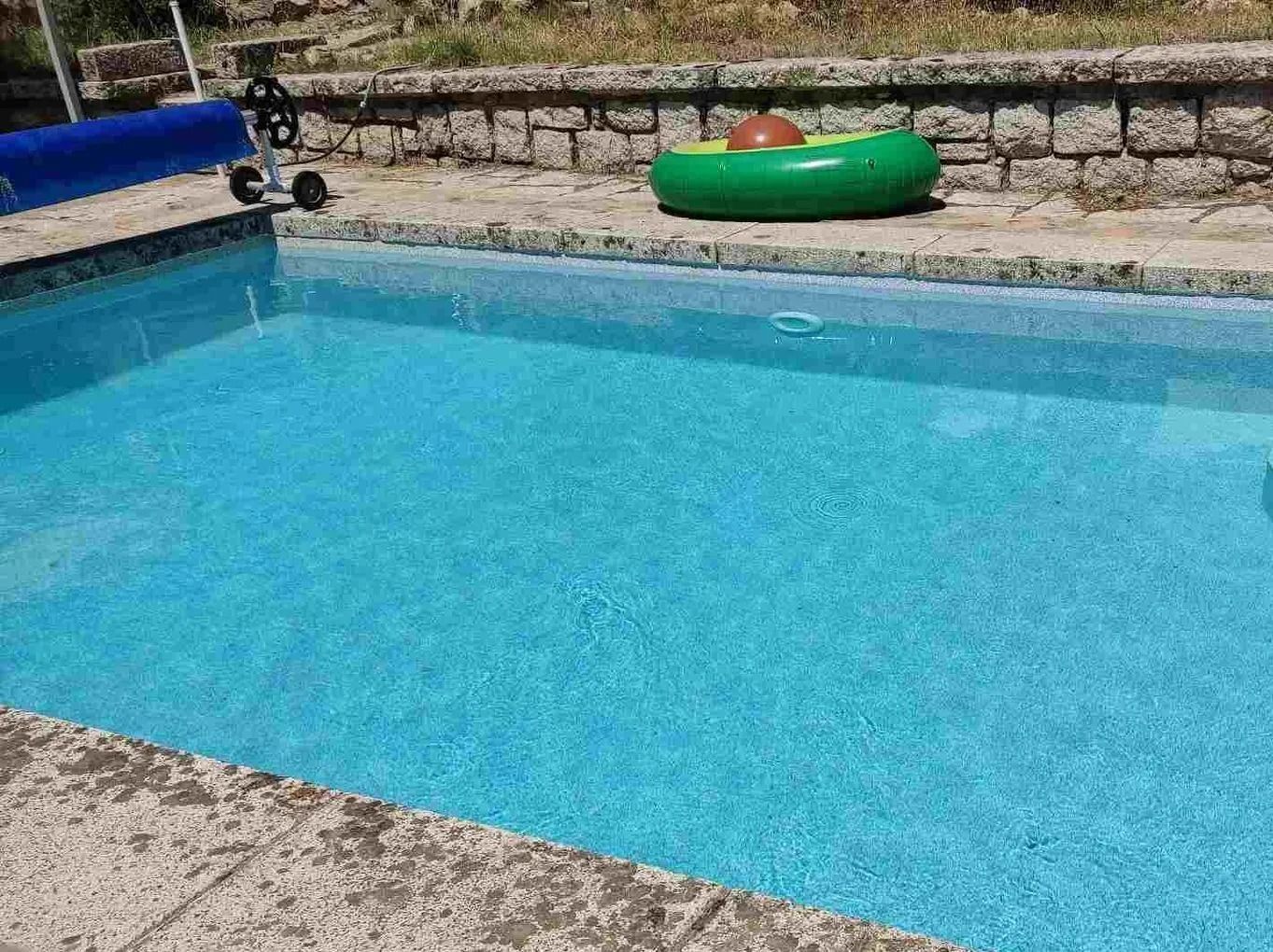 Una piscina de color azul claro con un anillo inflable verde y un muro de piedra como fondo.