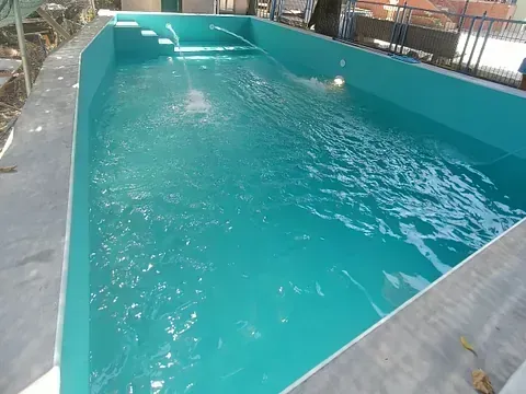 Una piscina rectangular de color turquesa con fuentes de agua y escalones, al aire libre.