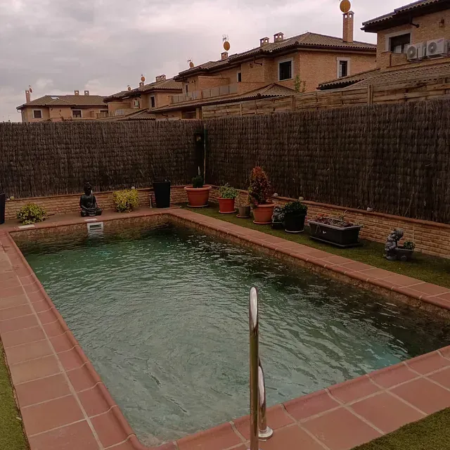Una gran piscina rodeada de plantas en macetas y una valla.