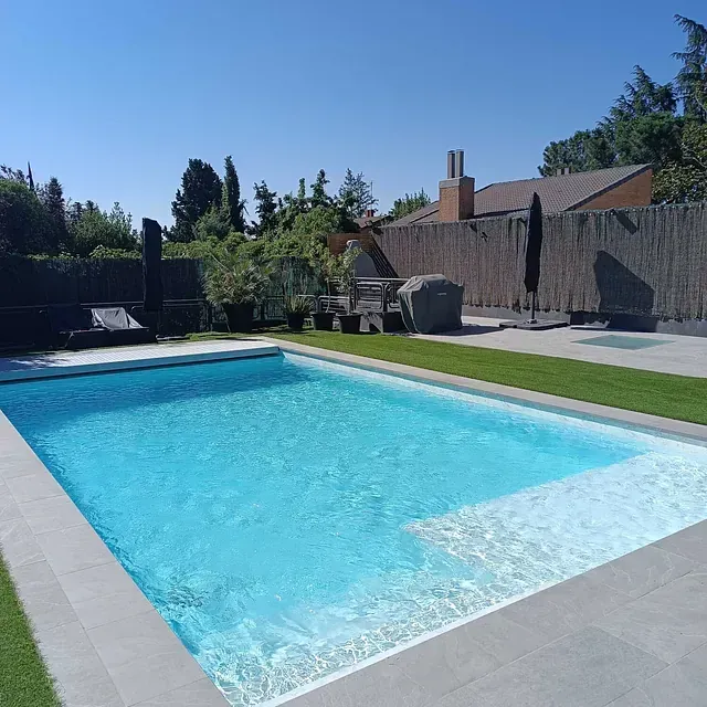 Una gran piscina rodeada de césped y una valla.