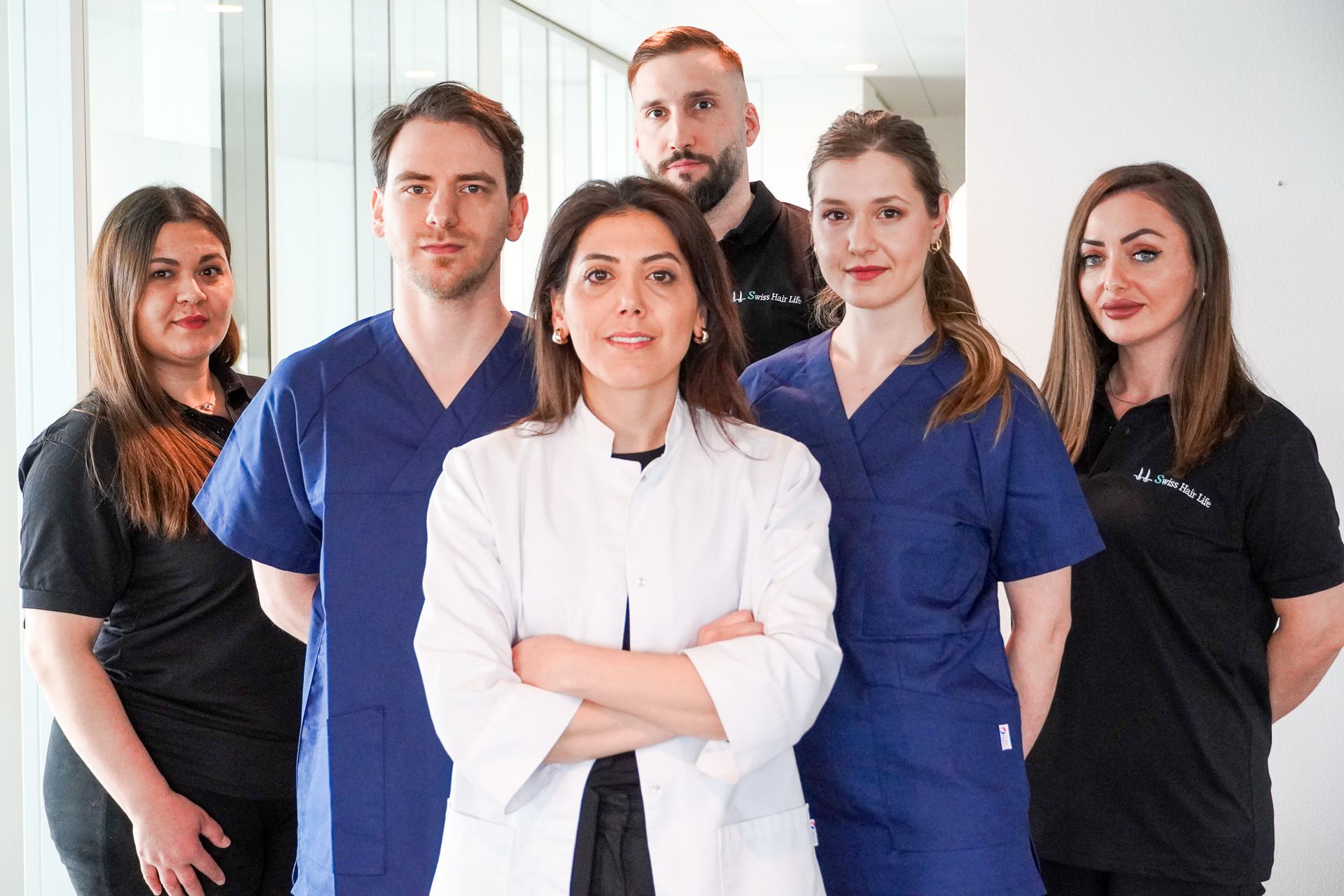 Team von Medizinern in einer Klinik. Weißer Laborkittel, blaue OP-Kleidung, neutrale Umgebung.