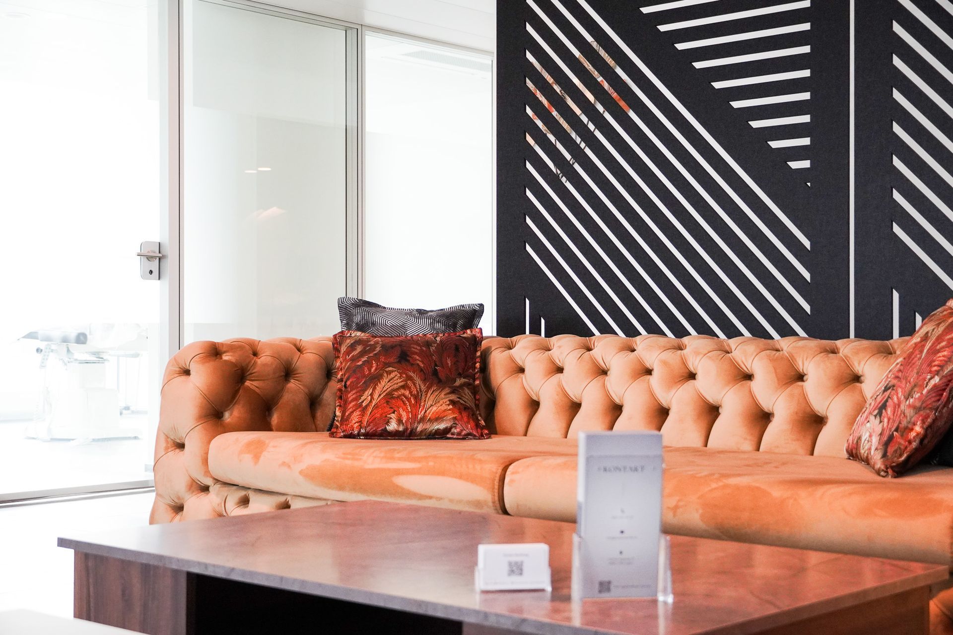 Orangefarbenes Sofa mit Polsterknöpfen und gemusterten Kissen vor einer schwarz-weißen grafischen Wand.