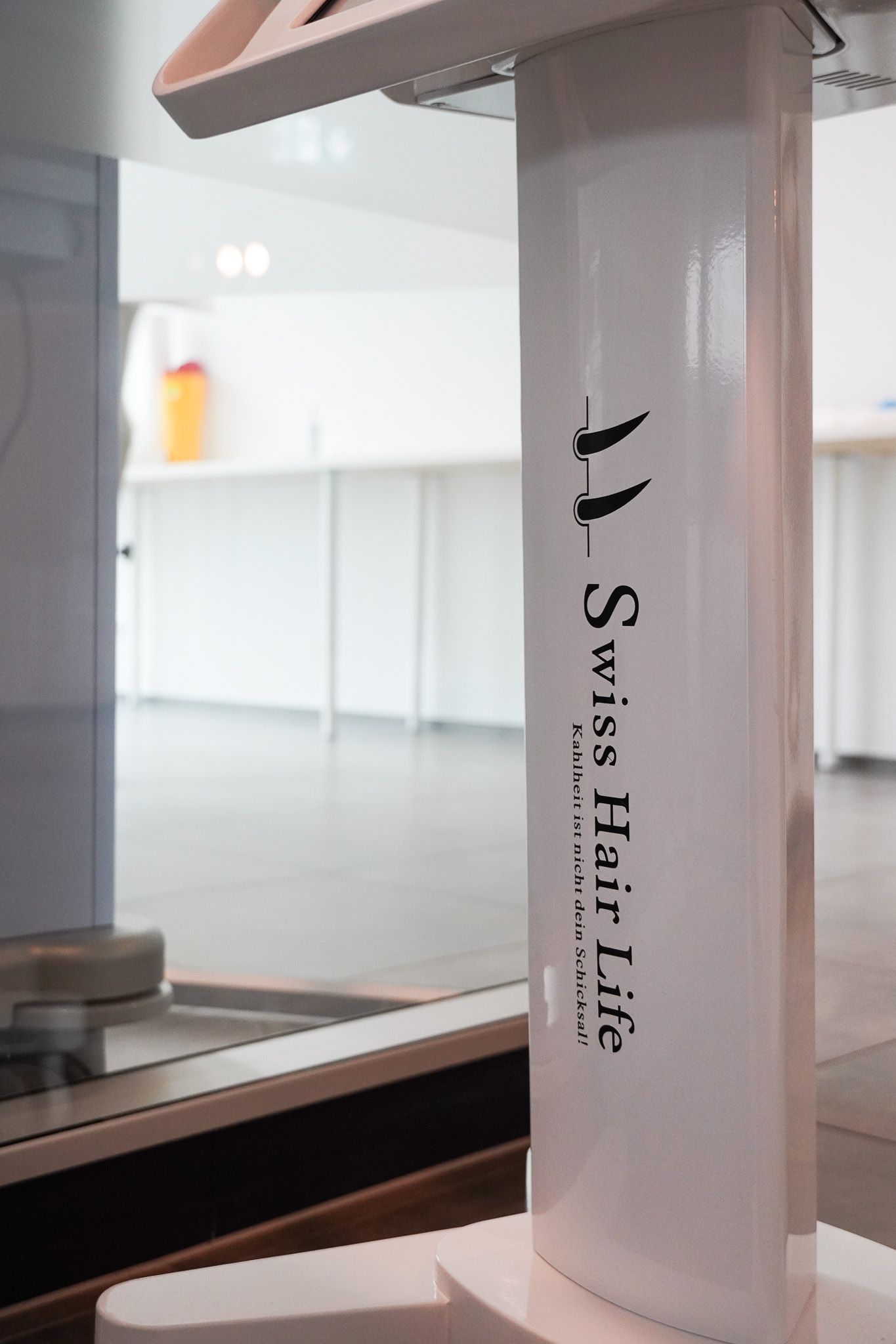 Weiße Säule mit „Swiss Hair Life“-Logo in einem hellen, modernen Raum.