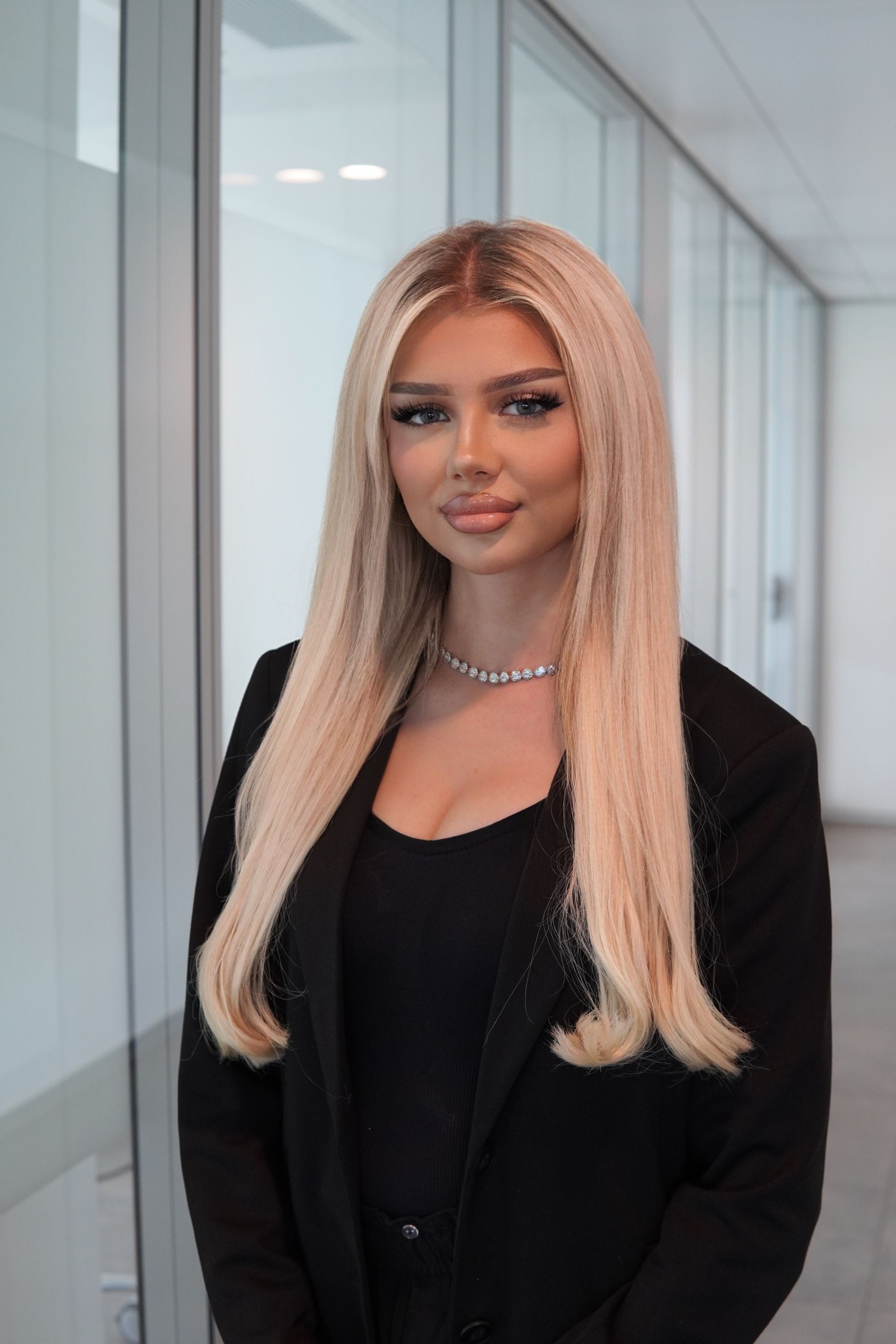 Frau mit langen braunen Haaren lächelt, trägt ein schwarzes Hemd und steht in einem Büro.