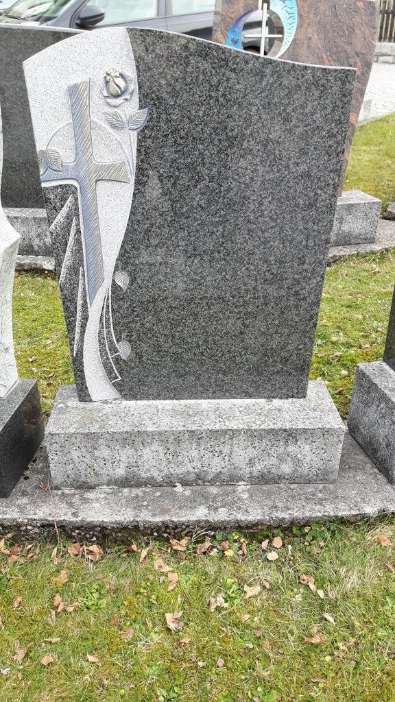Grauer und schwarzer Granitgrabstein mit eingraviertem Muster und einer Rose auf einem Sockel in einem grasbewachsenen Friedhof.